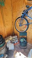 Fishing rods with reels leaning against wooden wall by bicycle wheel, several fishing storage boxes on floor