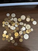 Photo showing an assortment of 49 coins in different colors and sizes, laid out on a dark surface.