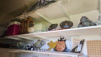 Wide shelf view showing ceramic frog figures, skunk figurines, ceramic fish wall hanging, ladybug and fish figures, planter containers, metal lanterns, and a purple cooler.