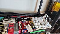 Overview photo of golf clubs mostly shafts and heads visible with golf ball boxes and loose balls on table surface.