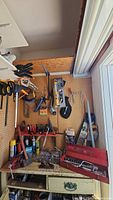 Wide view of pegboard with clamps, saws, hardware, toolbox and tools on shelf