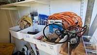 Wide view of plastic bins containing orange and yellow extension cords, assorted nails, drill bits, and blue zip ties on shelves.