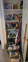 Closet shelf fully stocked with assorted cleaning bottles, sprays and cleaning tools like mops and sponges