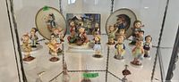 Shelf display of 17 porcelain Hummel figurines and two plates