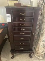 Front view of the dark wood jewelry armoire with multiple drawers and side panels closed.