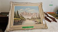 Full view of framed landscape oil painting showing mountain, trees, river and ornate frame.
