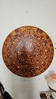 Front view of large circular Mayan calendar wooden mosaic mounted on wall.