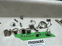 Full lot with six rings, two pins, and one pendant necklace laid out on white surface with green tape labeled Mexican silver.