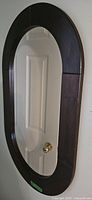 Large oval wall mirror with dark wood frame hanging on white door, showing reflective surface and frame design