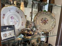 Display of plates, porcelain boots, and Royal Vienna candy dish in glass cabinet