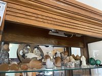Wide shot of various stone carvings and figurines on glass shelf with mirrored background, showing diverse shapes and colors.
