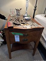 Top and front view of wooden side table with items on top including coins, a glass, and collectibles, showing drawer and inset leather top.