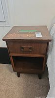 Single brown wood bedside table with drawer and open shelf beside a bed
