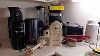 Wide view of all the kitchen appliances on countertop including can opener, kettle, mixers, toaster, coffee makers, coffee grinder, etc.