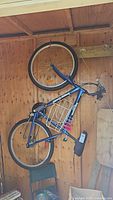 Side view of the blue Supercycle SC1800 mountain bike hung on a wooden wall, showing the entire bike including tires, frame, seat, and gear system.