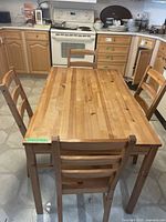 Wood kitchen table with four matching chairs set on a tiled kitchen floor, showing the rectangular table and chair backs.