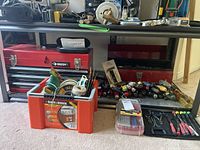 Bottom shelf showing both red metal toolboxes, Black & Decker plastic toolbox with cords and string, ColdHeat soldering tool case, small clear bit organizer and precision screwdriver pouch.