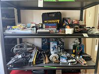 Two shelves filled with assorted power and hand tools including jigsaw, electric sanders, hammers, levels, and cases of tools.