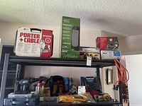 Shelf with Porter Cable nailing machine box, Hunter tower heater box, safety glasses, remote thermometer, and face shields.