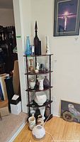 Full view of wooden corner shelf holding multiple vases of different styles and sizes including pottery, glass, and ceramic pieces with a framed wall art in the background