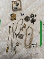 Full view of vintage costume jewelry including necklaces, earrings, pins, and brooches laid on white quilted surface.