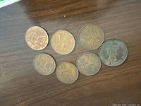 Seven vintage coins laid out on a brown surface showing front and back of UK pennies and the Canadian coronation medal.