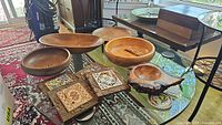 Five wood serving bowls, three trivets on a glass table with surrounding furniture visible