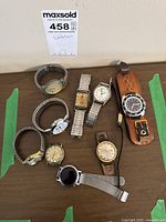 Photo of eight wristwatches arranged on a table showing varying styles and bands, including metal expansion, leather straps, metal mesh strap, and a leather cuff mounting.