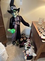 Photo showing full Halloween witch figure, two teddy bears, Minnie Mouse plush, and dog with maracas plush in a room corner.