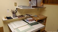 Overview of art supplies on shelves and desk including paper, brushes, charcoal, and sketch pads