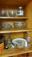 Glass bowls and jars on wooden shelf, with some clear glass candle holders and a porcelain plate visible below.