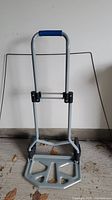 Front view of the foldable hand truck trolley with metal frame, plastic base, blue handle grip, and two wheels