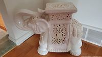 Front-side diagonal view of the white ceramic elephant garden stool showing carved patterns and trunk raised.