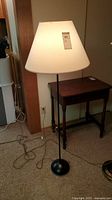 Floor lamp with white conical lampshade, black metal pole and round base, 55 inches tall, pull chain switch visible, cord on floor.