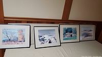 Four framed prints by B Gerstiver, arranged in a row on a beige surface with wooden wall background.