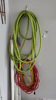Coiled green garden hose and red-yellow extension cords hung against a wall