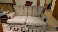 Front view of Sears loveseat sofa with textured fabric upholstery, cushioned backrest and two seat cushions, pleated skirt base.