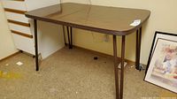 Photo of the full table showing wood-grain laminate top with distinct center insert and four V-shaped metal hairpin legs.