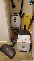 Miele canister vacuum body, hose, box of vacuum bags and attachments on floor