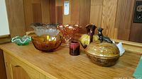 Full view of the lot on a wooden counter showing various bowls, pottery and glass items including a nut bowl with squirrel and multiple carnival glass bowls.