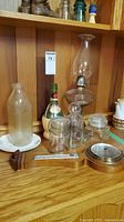 Photo showing vintage bottles including an oil lamp and jars on wooden shelf.
