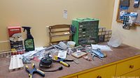 View of workbench surface holding various tools including clamps and screwdrivers, a green multi-drawer organizer, wooden tiered rack, and boxes of hardware supplies.