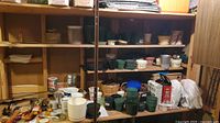 Wide view of storage shelving with multiple plastic and ceramic plant pots, cans of plant food, and other gardening supplies