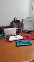 Overview photo of all seven handbags, purses, and clutches on wooden surface showing variety in styles and colors