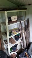 White metal shelving unit with four shelves, some dirt and minor rust, located inside shed with miscellaneous items on shelves.