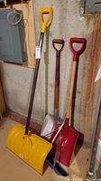 Four shovels of various types leaning against a wall indoors.