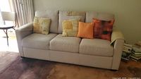 Front view of fabric sofa with four throw pillows arranged on the back cushions, angled to show left armrest and seat cushions