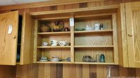 Wooden cabinetry with shelves displaying several teacups, a pitcher, and decorative items.