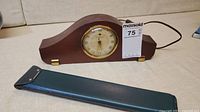 Side view of vintage electric mantel clock with wooden case and green leather slide rule case lying in front