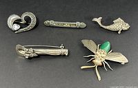 Five sterling silver brooches laid out for overview